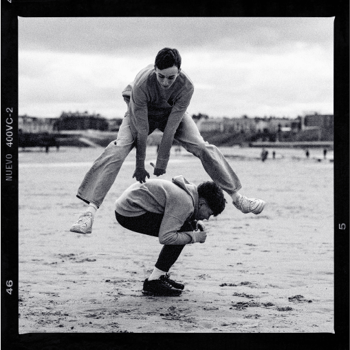 Two people playing on sand. One is jumping over the other.